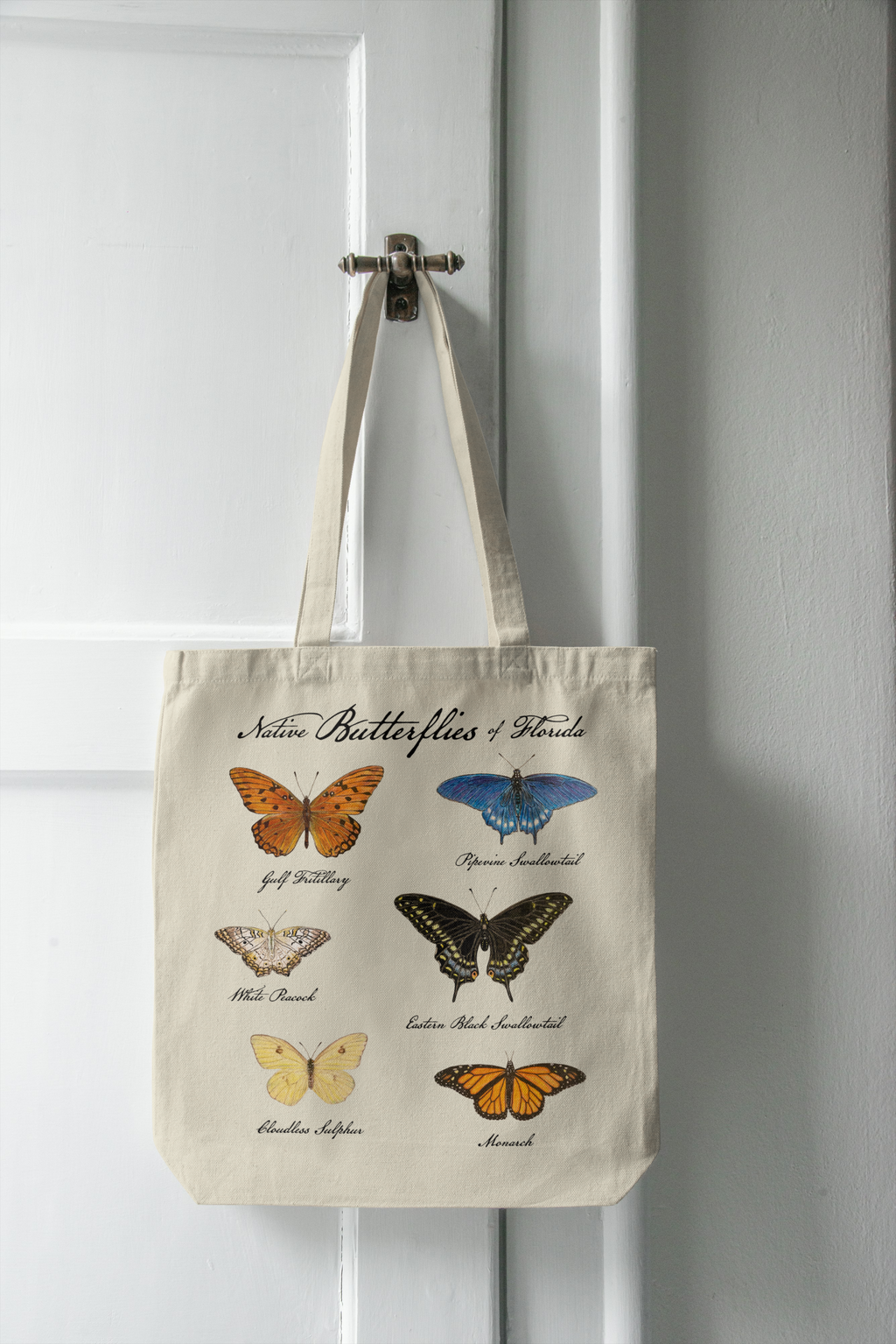 Tote bag with butterfly illustrations hanging on a white door