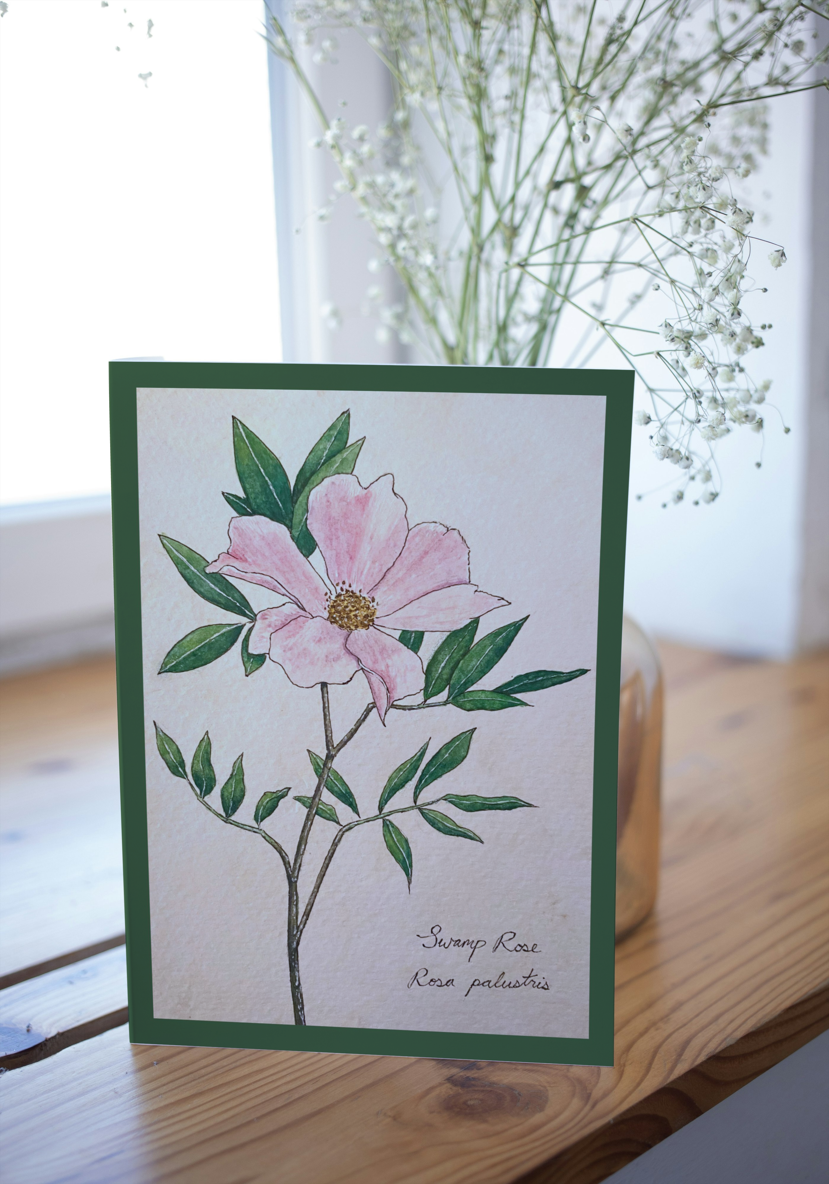 Card with a pink flower illustration on a wooden surface with a blurred background