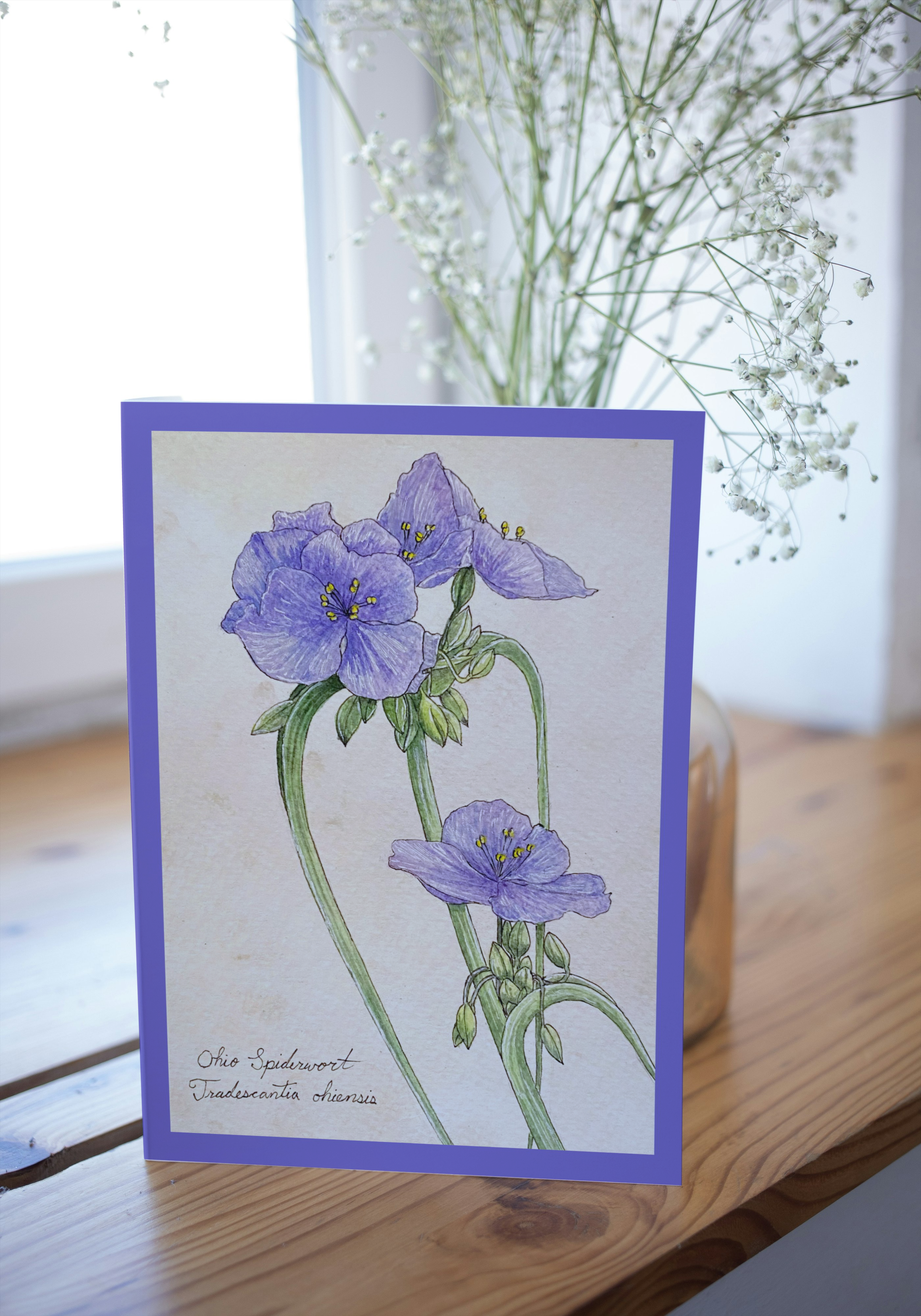 Card with purple flower illustration on a wooden surface with flowers in the background