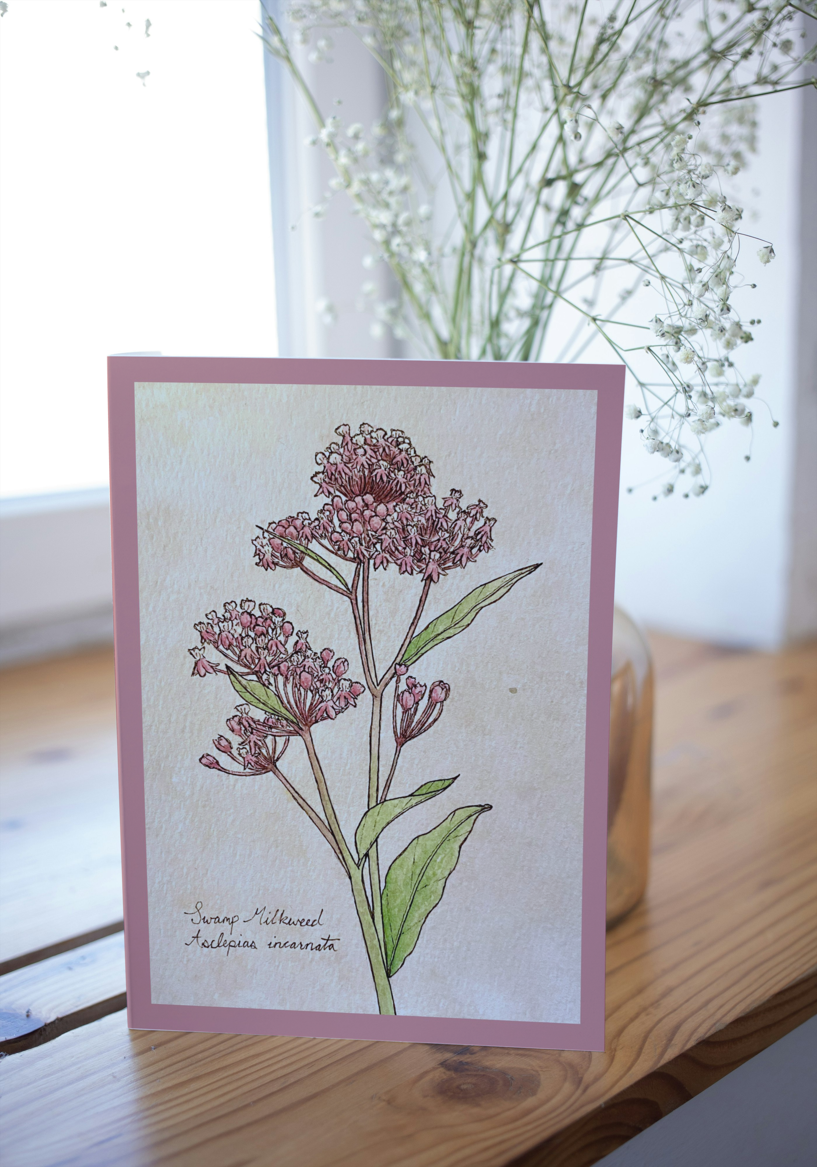 Card with botanical illustration of pink flowers on a wooden surface with blurred background
