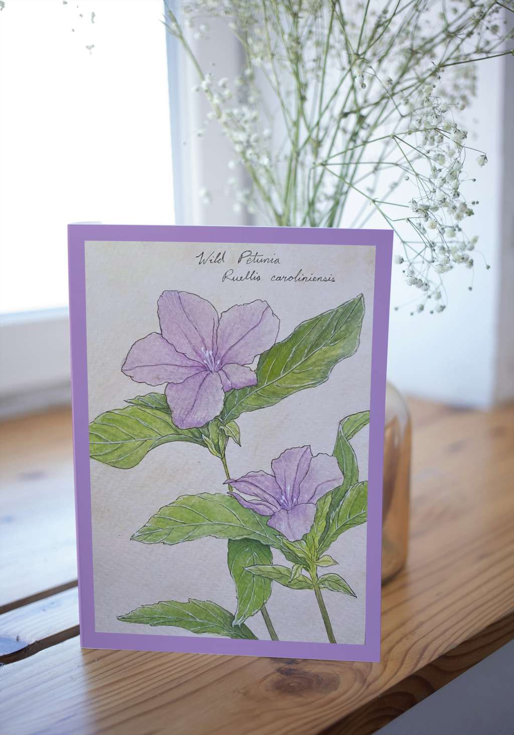 Card with purple flowers and green leaves on a wooden surface with a blurred background