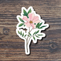 Floral sticker with pink flower and green leaves on a wooden surface