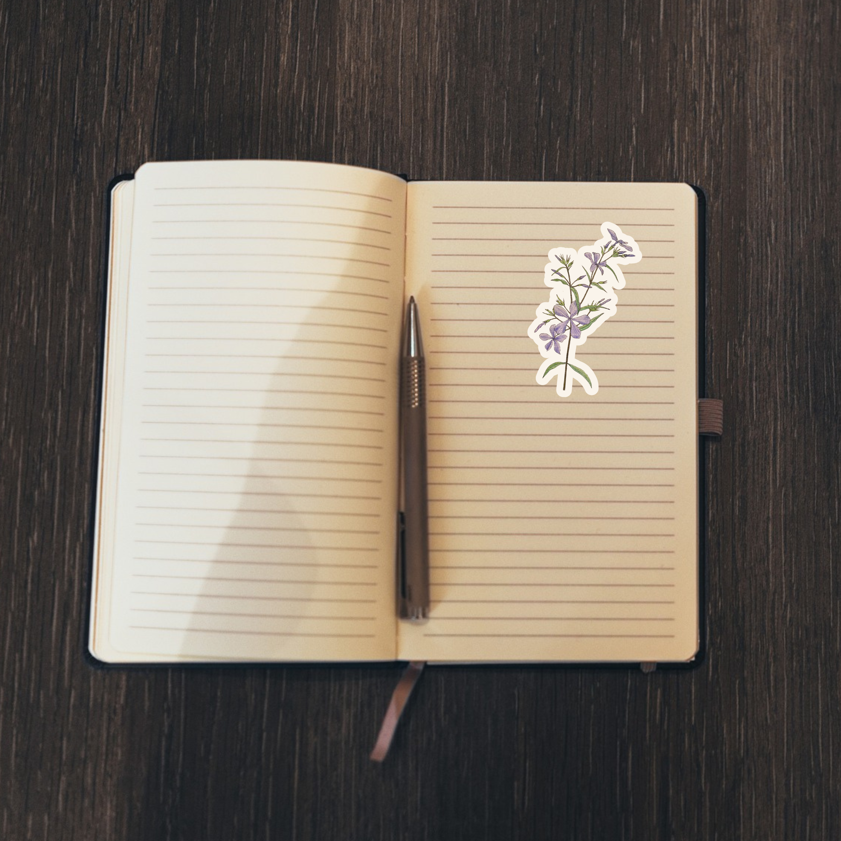 Open notebook with a pen and a floral sticker on a wooden surface