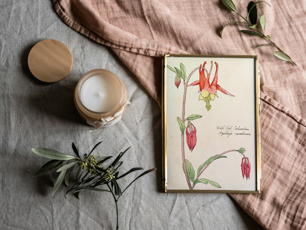 Framed botanical print of flowers on a textured surface with a candle and greenery