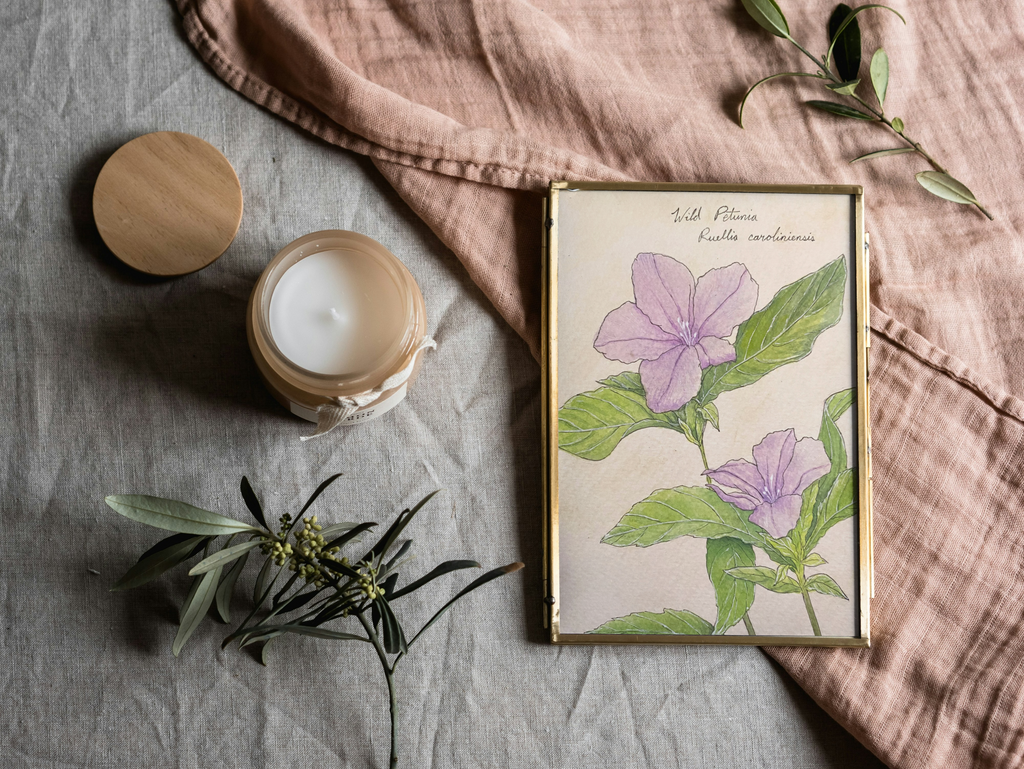 Framed botanical print on a textured surface with a candle and greenery
