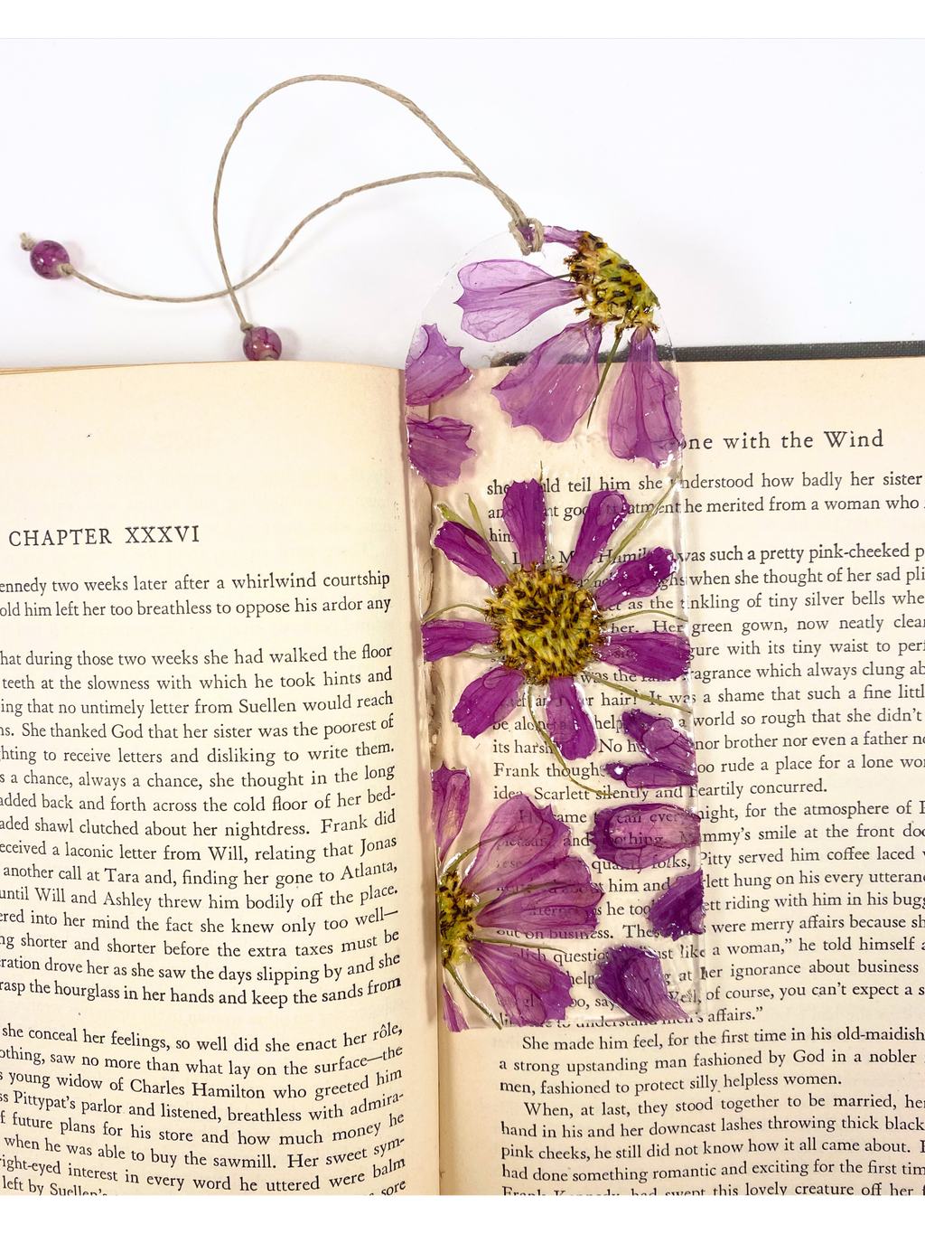 A bookmark featuring pressed purple flowers with yellow centers displayed on an open book.