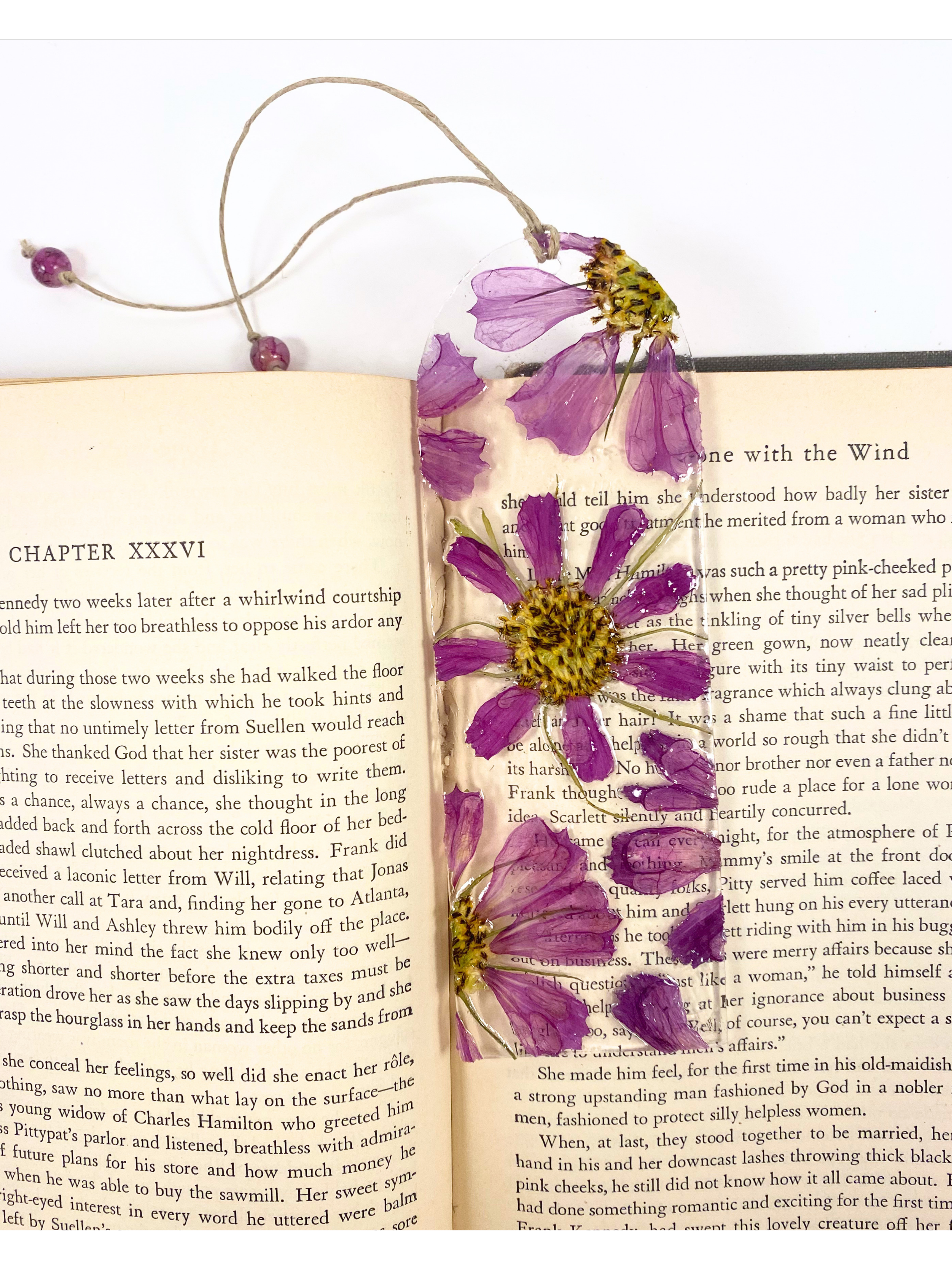 A bookmark featuring pressed purple flowers with yellow centers displayed on an open book.