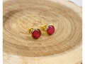 A pair of gold stud earrings containing deep pink flower petals, displayed a wooden slice background.
