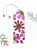 A bookmark featuring pressed purple flowers with yellow centers on a white background with decorative leaves at the corners.