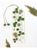 A bookmark featuring clover flowers and leaves, displayed on a white background with decorative leaves in the corners. 