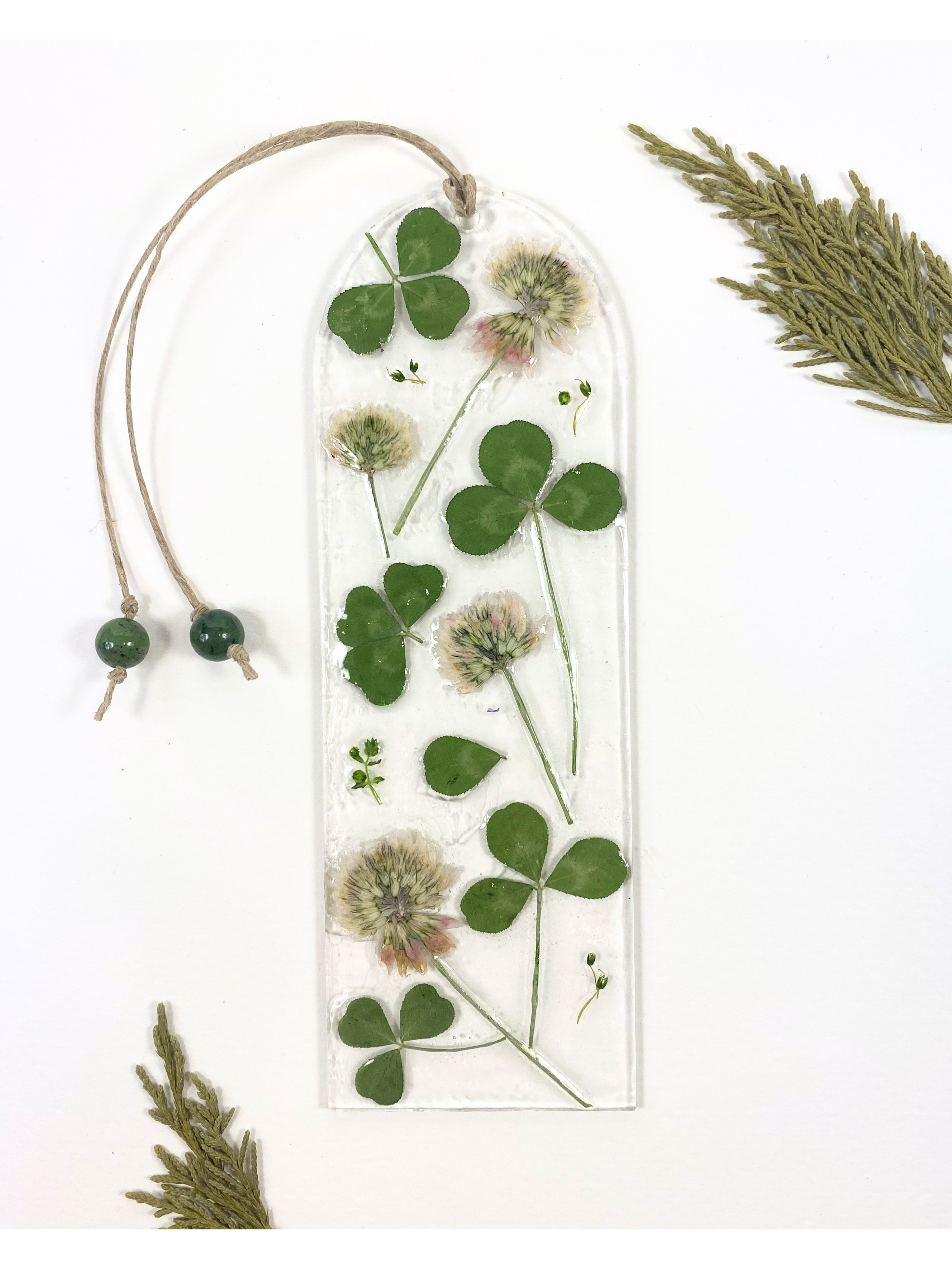 A bookmark featuring clover flowers and leaves, displayed on a white background with decorative leaves in the corners. 