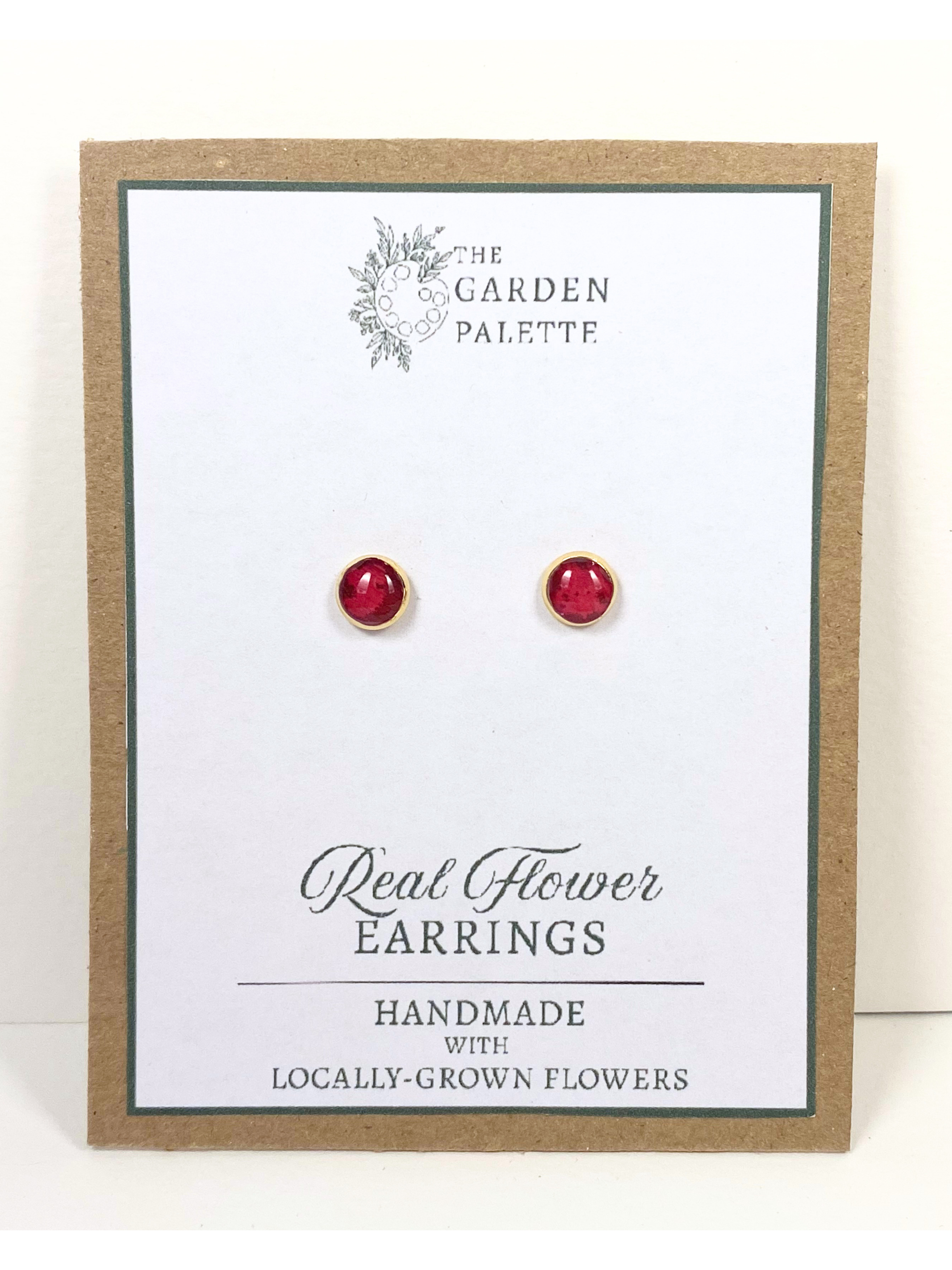 A pair of handmade deep pink flower stud earrings displayed on a white card with a kraft paper border. The card is branded 'The Garden Palette' and reads 'Real Flower Earrings'.