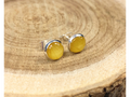 A pair of round silver stud earrings containing yellow flower petals, displayed on a rustic wood slice background. 