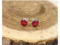 A pair of round silver stud earrings containing deep pink flower petals, displayed on a natural wood slice background.