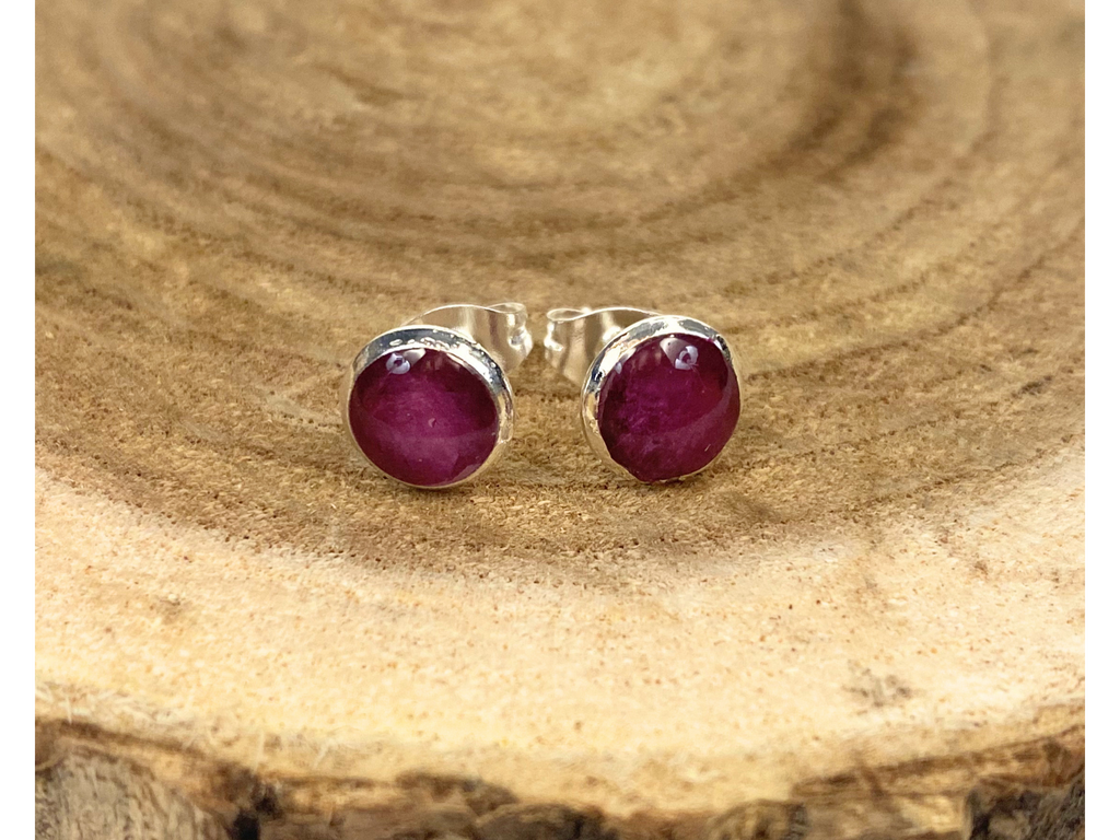 A pair of round silver stud earrings containing purple flower petals, displayed on a rustic wood slice background.