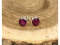 A pair of round silver stud earrings containing purple flower petals, displayed on a rustic wood slice background.