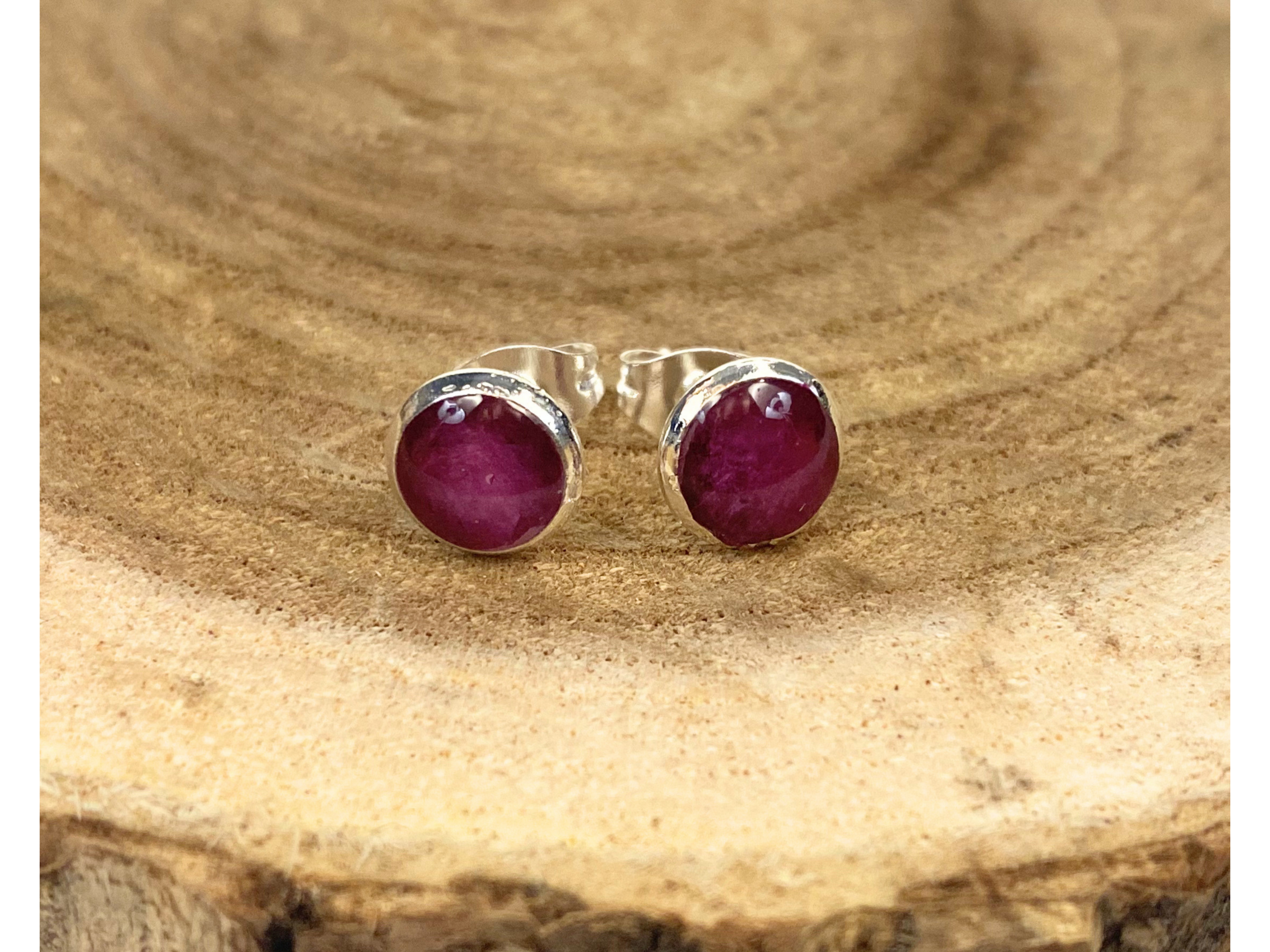 A pair of round silver stud earrings containing purple flower petals, displayed on a rustic wood slice background.