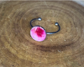 A silver-toned ring with a round bezel setting containing a pink petal, displayed on a rustic wood background.