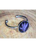 A silver-toned ring with a round bezel setting containing a blue flower petal on a black background, displayed on a rustic wood surface.