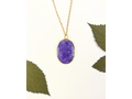 A gold chain necklace with an oval purple pendant containing dried flower inclusions, displayed on a white background with decorative green leaves.